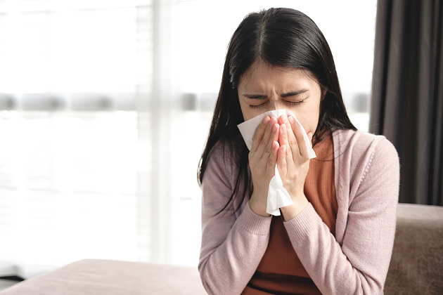 Woman sneezing into a tissue due to blocked nose.