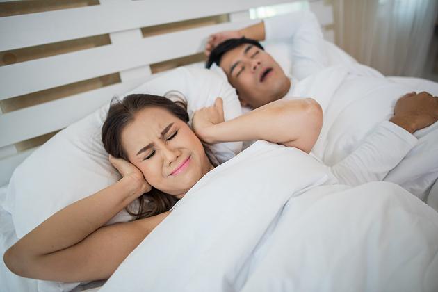 Woman covering ears while partner snores loudly in bed.